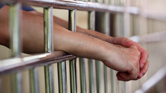 Man with hands through prison bars