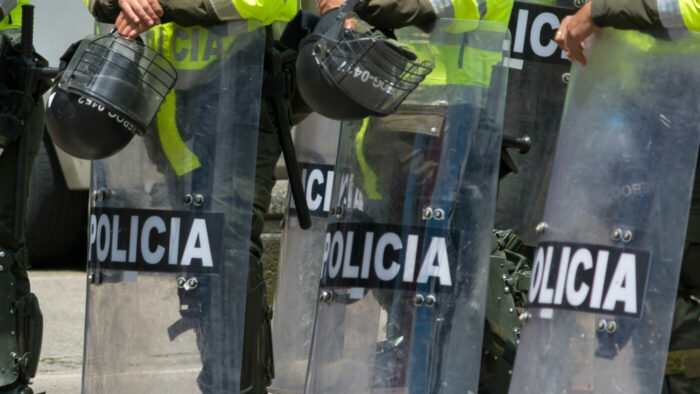 image shows police in riot gear with shields reading 'policia'