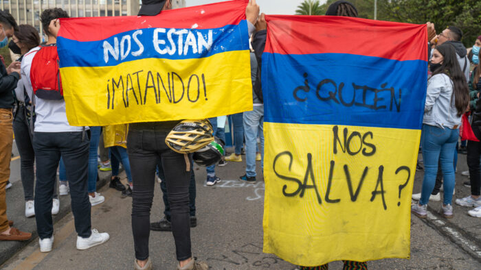 two people at a protest are holding Colombian flags