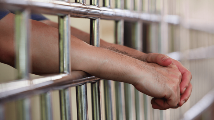 Person's hands through bars in cell